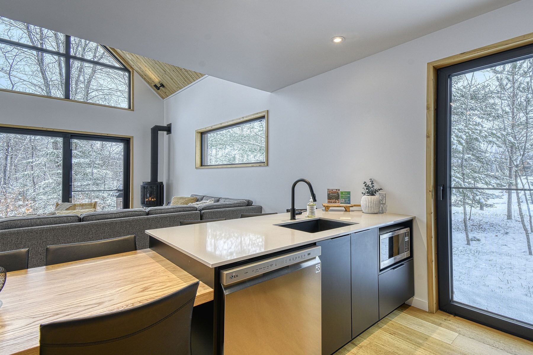 Una cocina moderna con lavavajillas, horno y estufa integrada. Hay un comedor con mesa y sillas, y ventanas amplias que ofrecen vistas a un paisaje nevado.