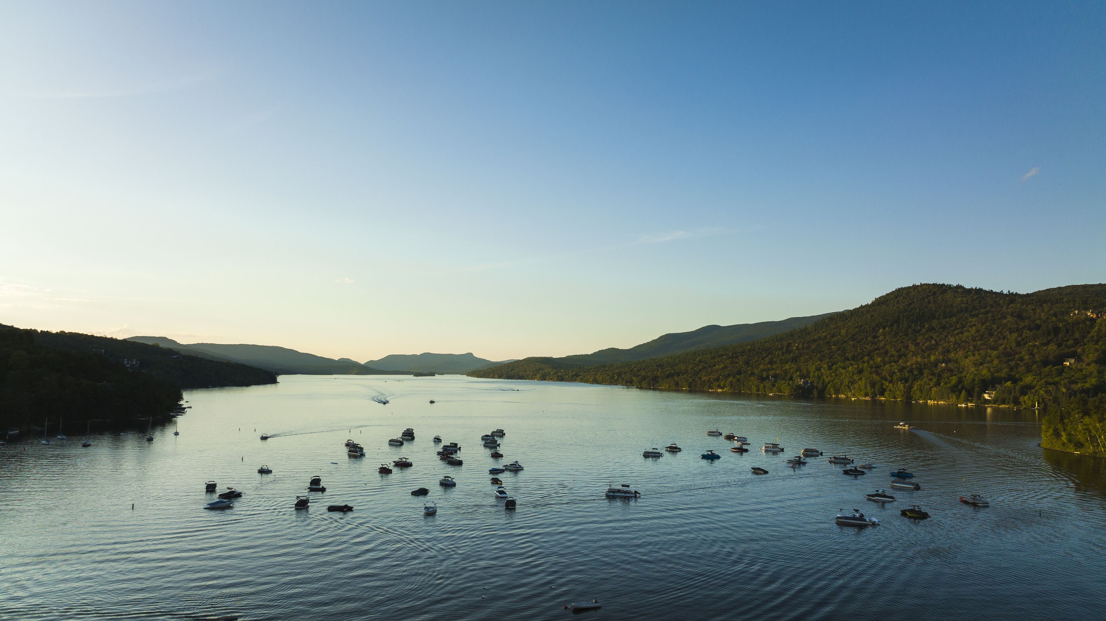A lake with numerous boats, surrounded by forested hills.