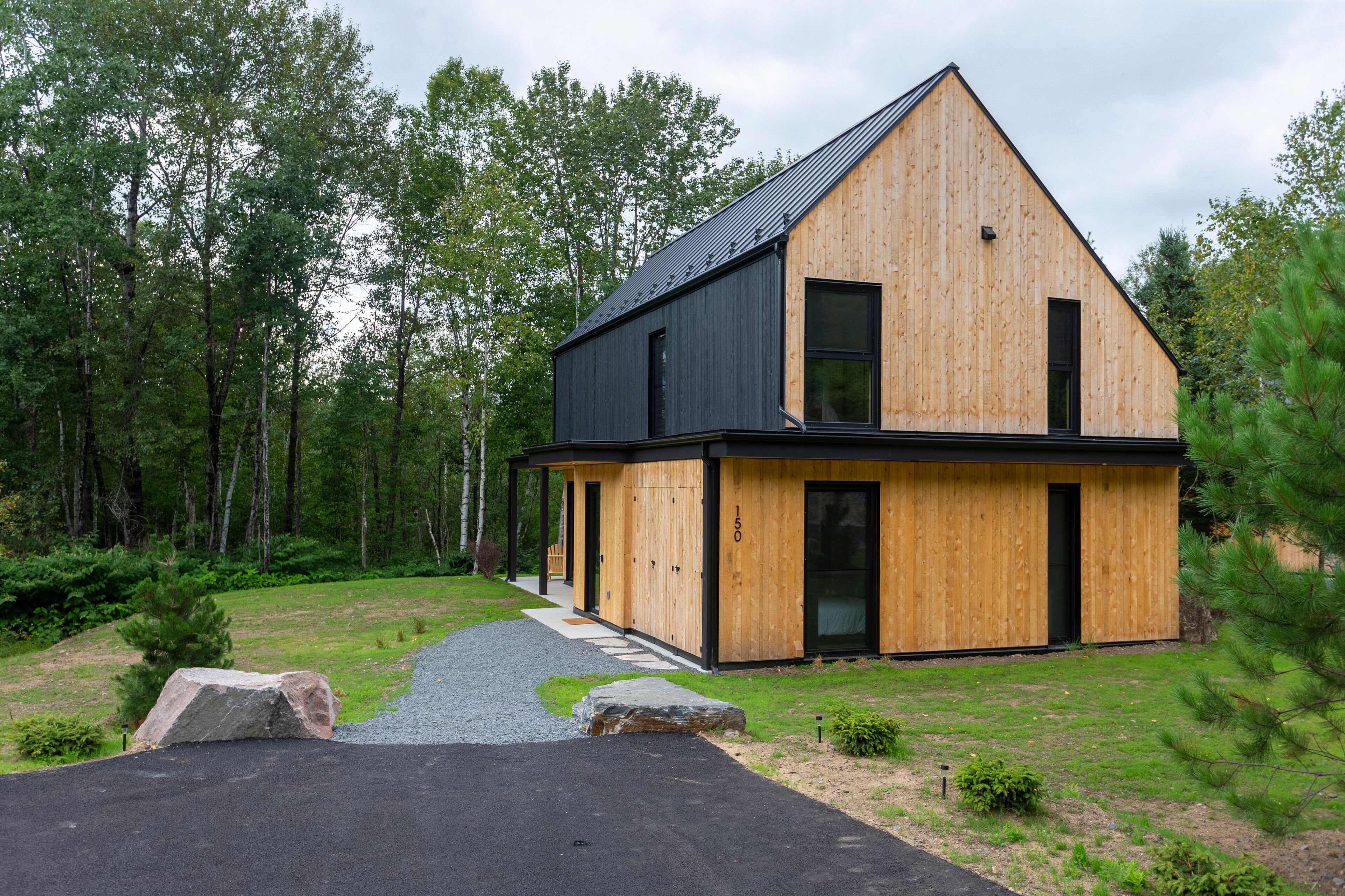 A modern wooden house with a black roof, a large front door, and a visible number "150" on the side.