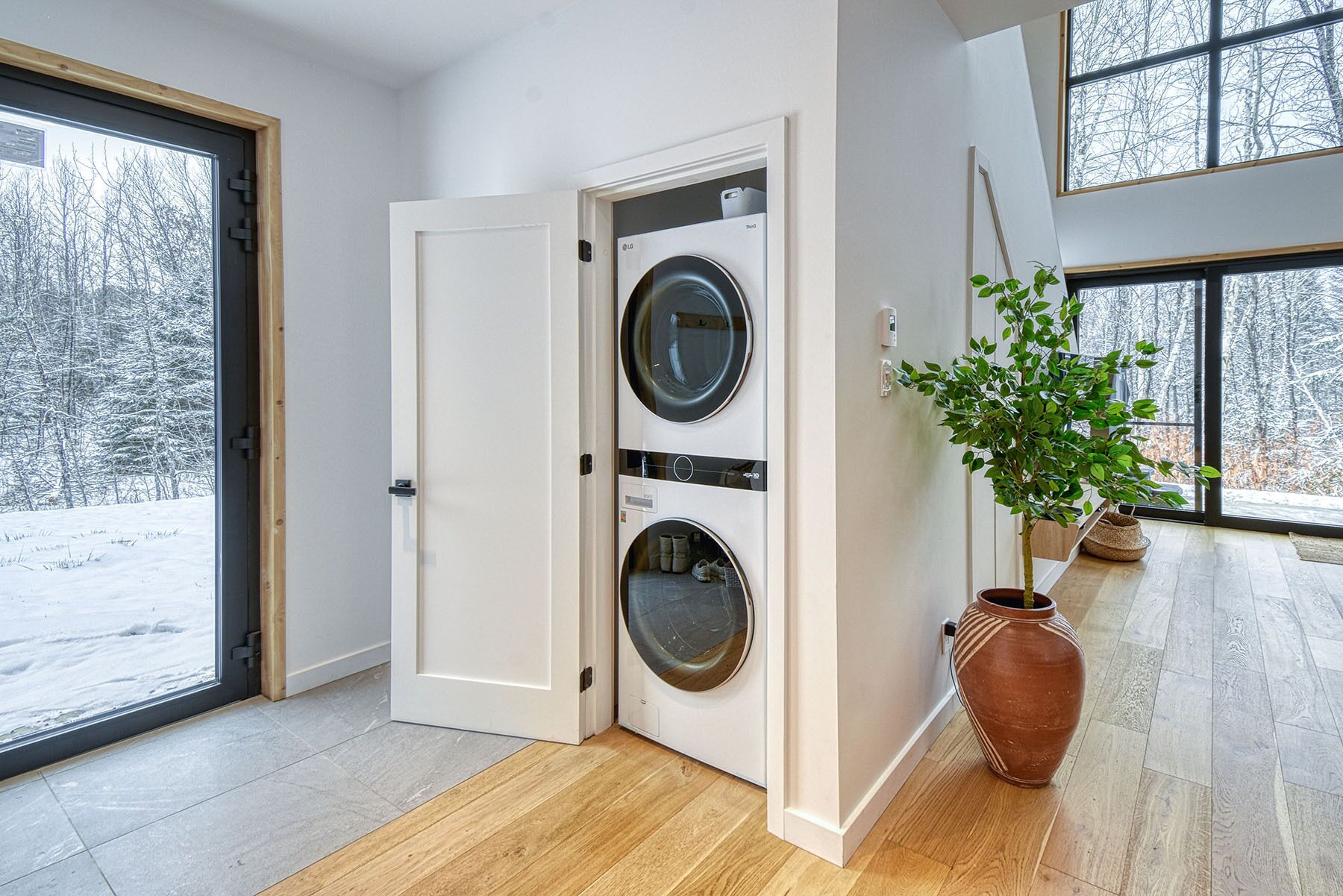 A room with a large window, a door leading to a laundry area with two washing machines, and a potted plant.