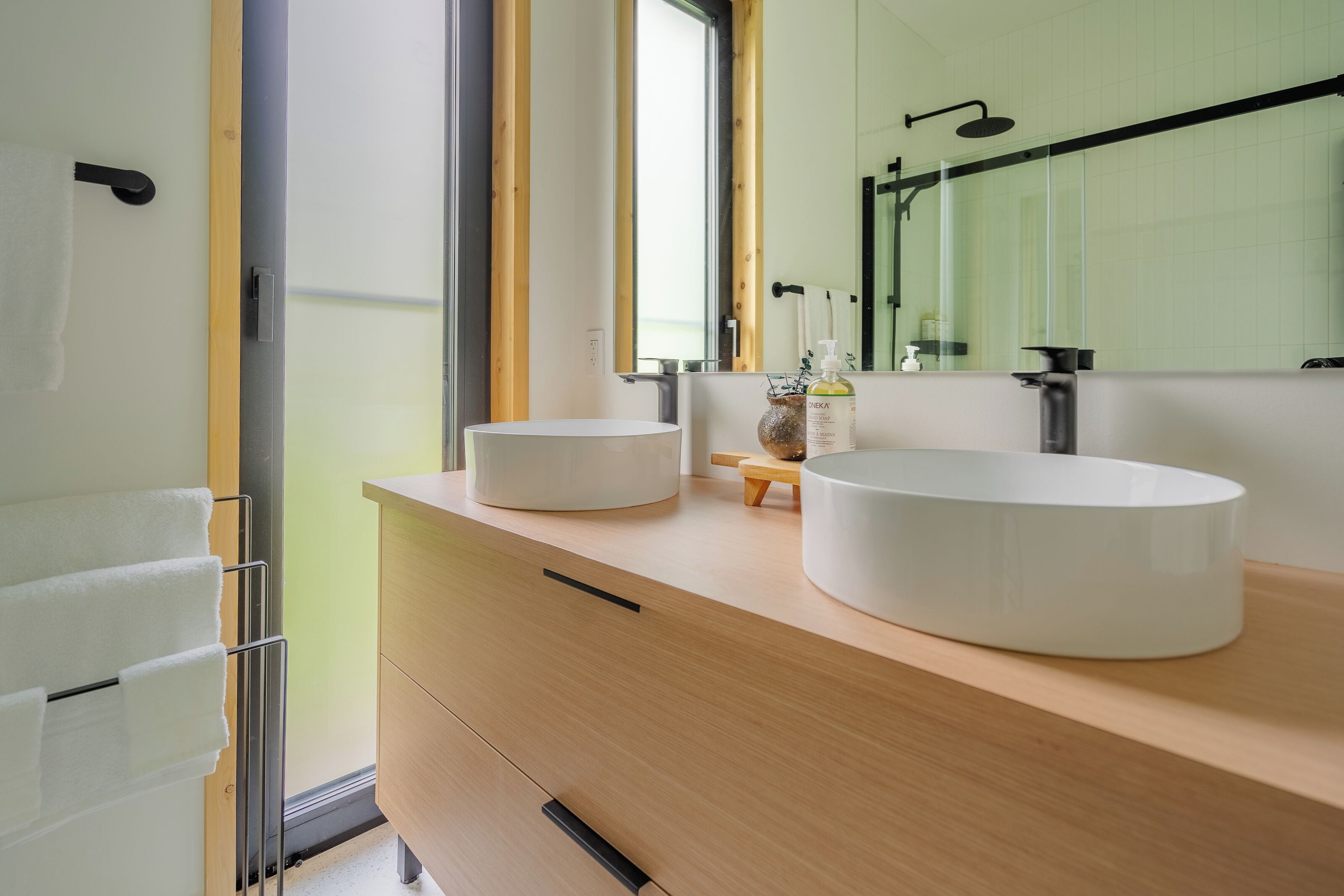 A modern bathroom with two round sinks, a wooden vanity, a mirror, and a glass shower enclosure.