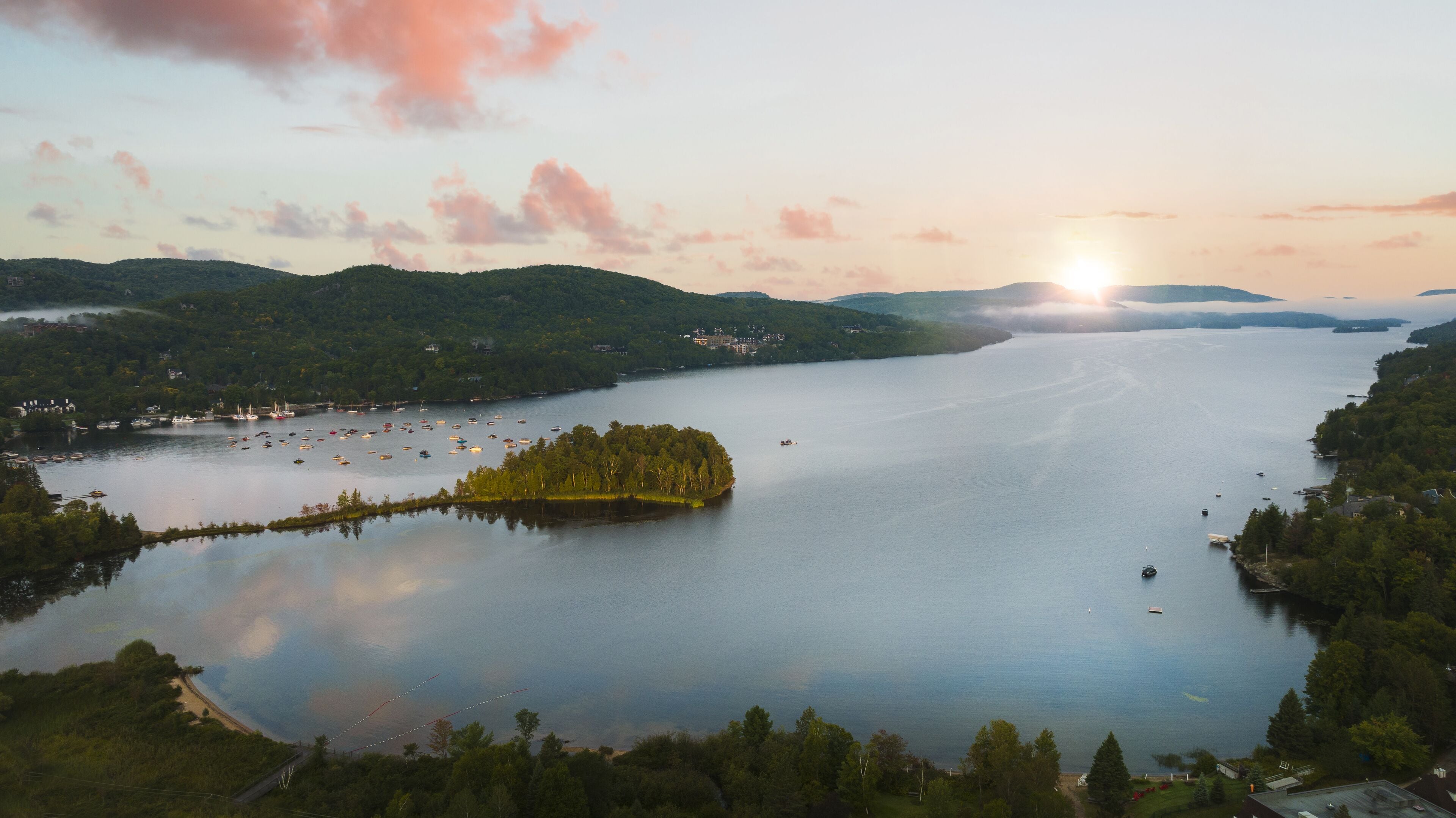 A lake surrounded by forested hills with boats and a small island.