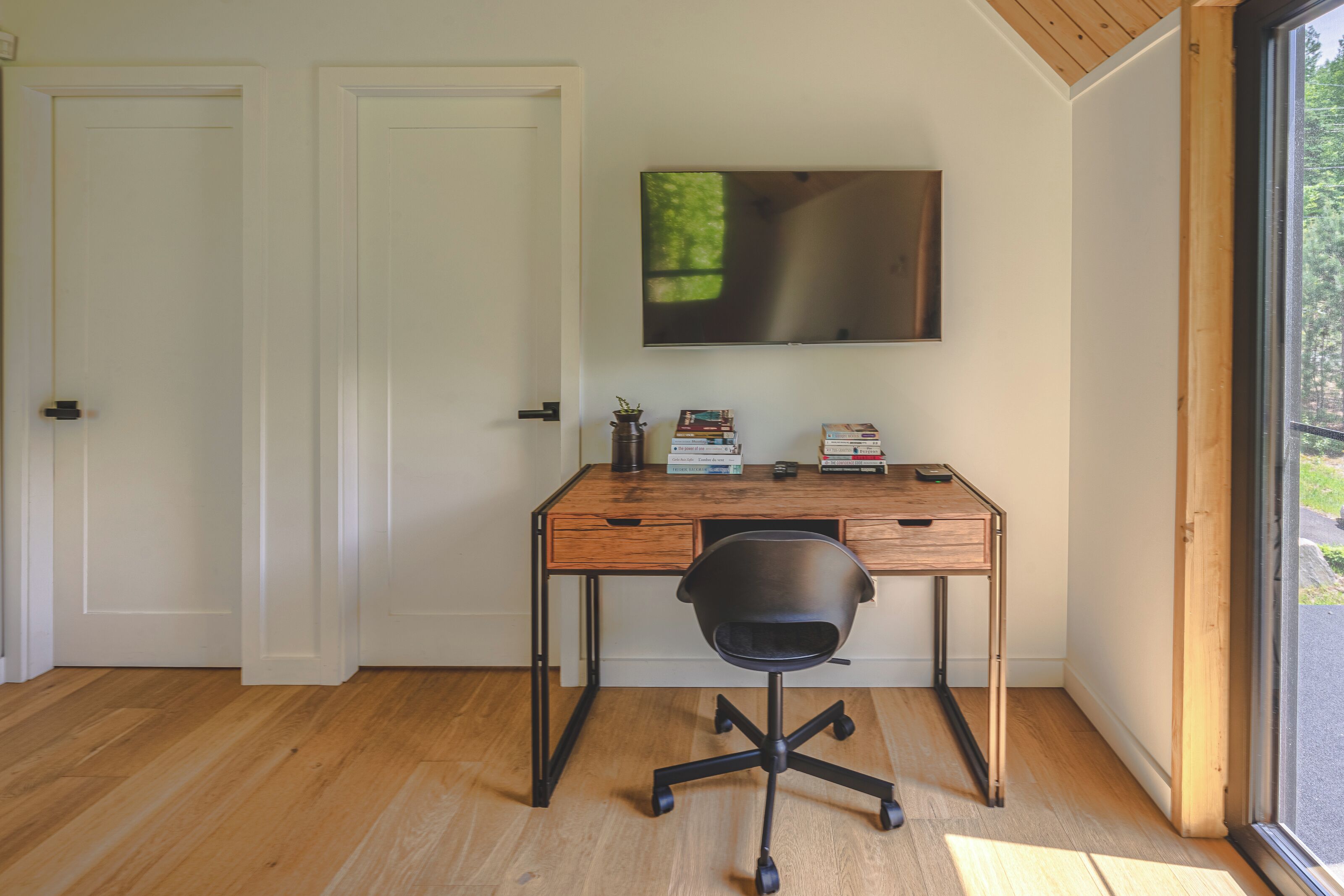 Ein moderner Arbeitsraum mit Schreibtisch aus Holz, schwarzem Bürostuhl und einem flach an der Wand befestigten Bildschirm.