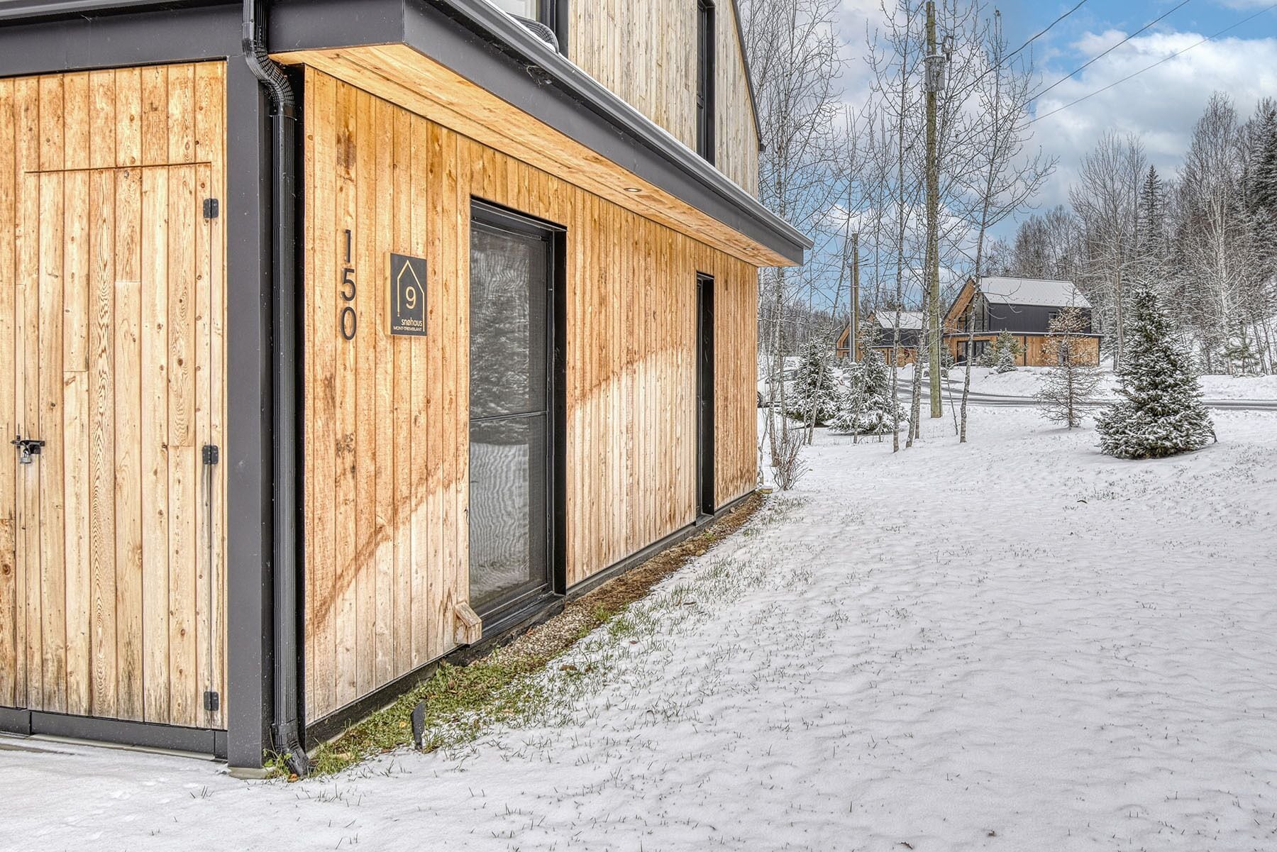 A modern wooden building with a large glass door, numbered 150, and a small sign indicating it is a sauna house.