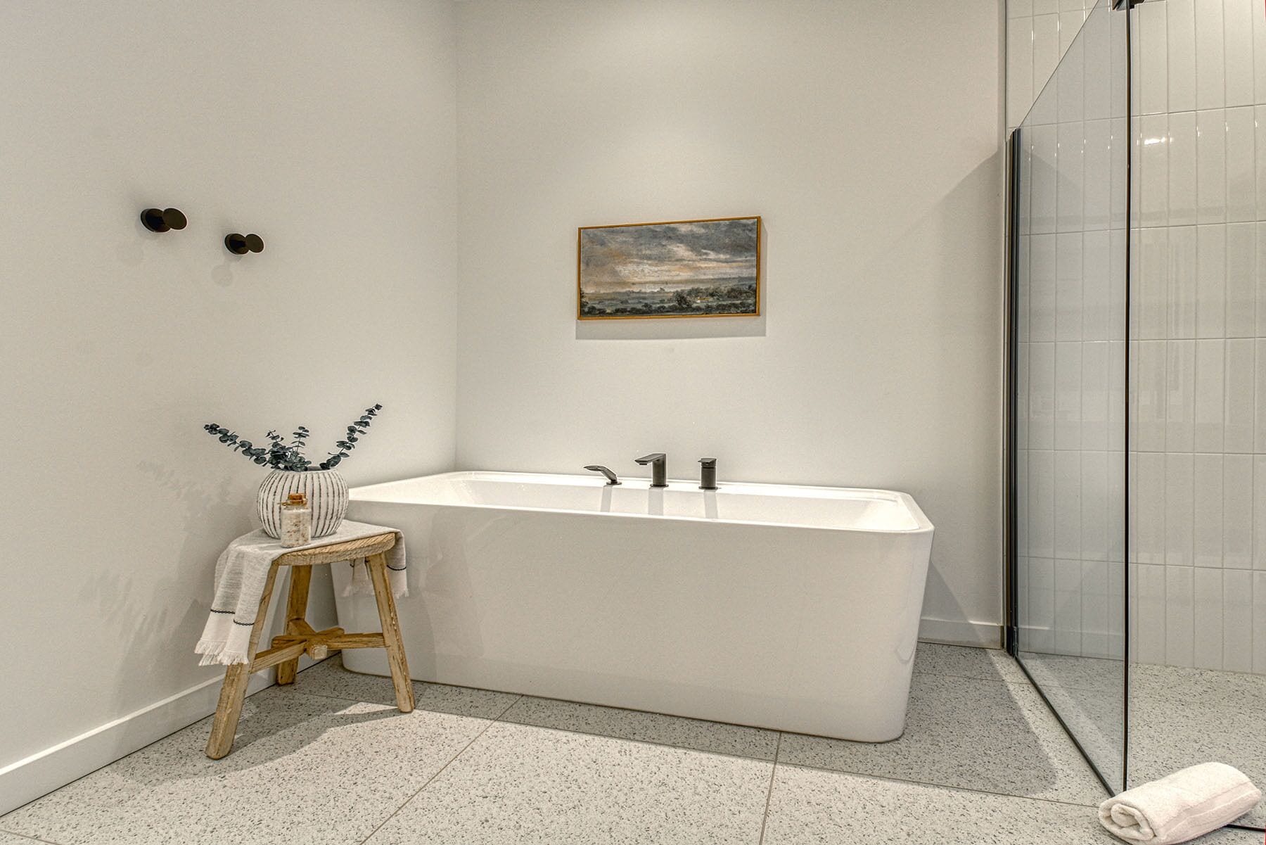 Ein modernes Badezimmer mit einer freistehenden Badewanne, einem kleinen Hocker mit einem Handtuch und einem Bild an der Wand.