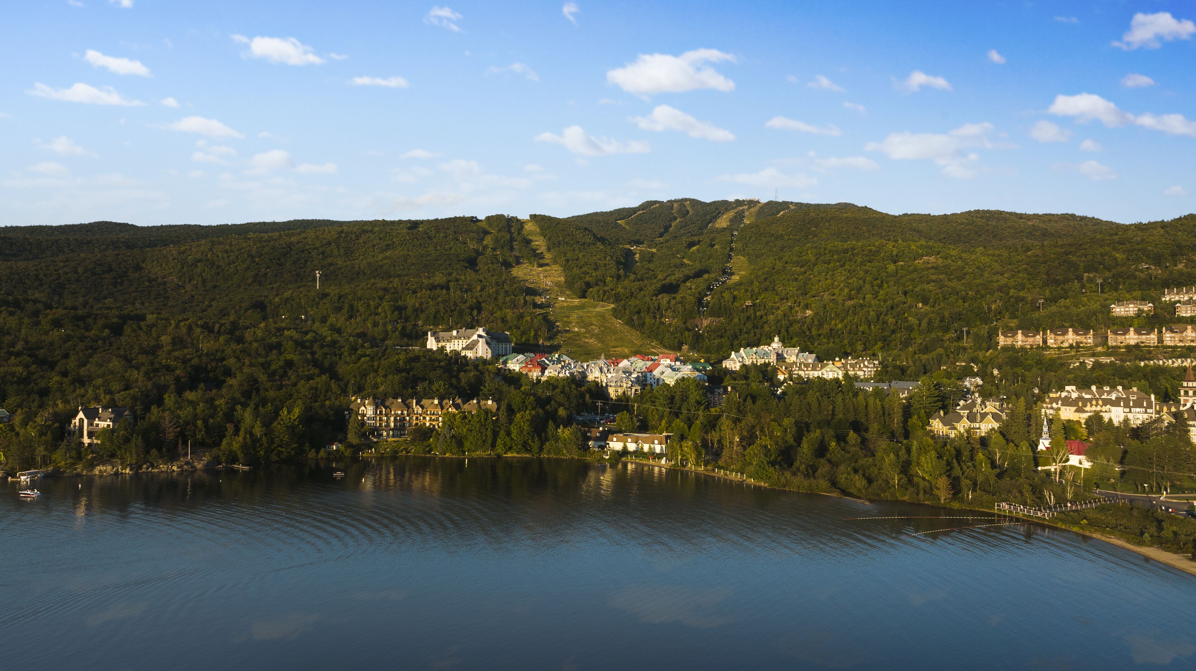 A lakeside town with buildings on a hillside, a clear sky, and calm water.