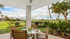 Un patio techado con una mesa redonda dispuesta para cuatro personas, rodeado de sillas, con vistas a un césped cuidado y edificios a la distancia.