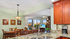 Una cocina con encimera de granito, pileta de acero inoxidable, armarios de madera y ventilador de techo.