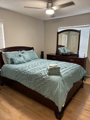 A bedroom with a bed, a dresser, a mirror, and a ceiling fan.