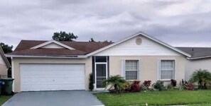 A single-story house with a garage, a front door, and a small front yard with plants.