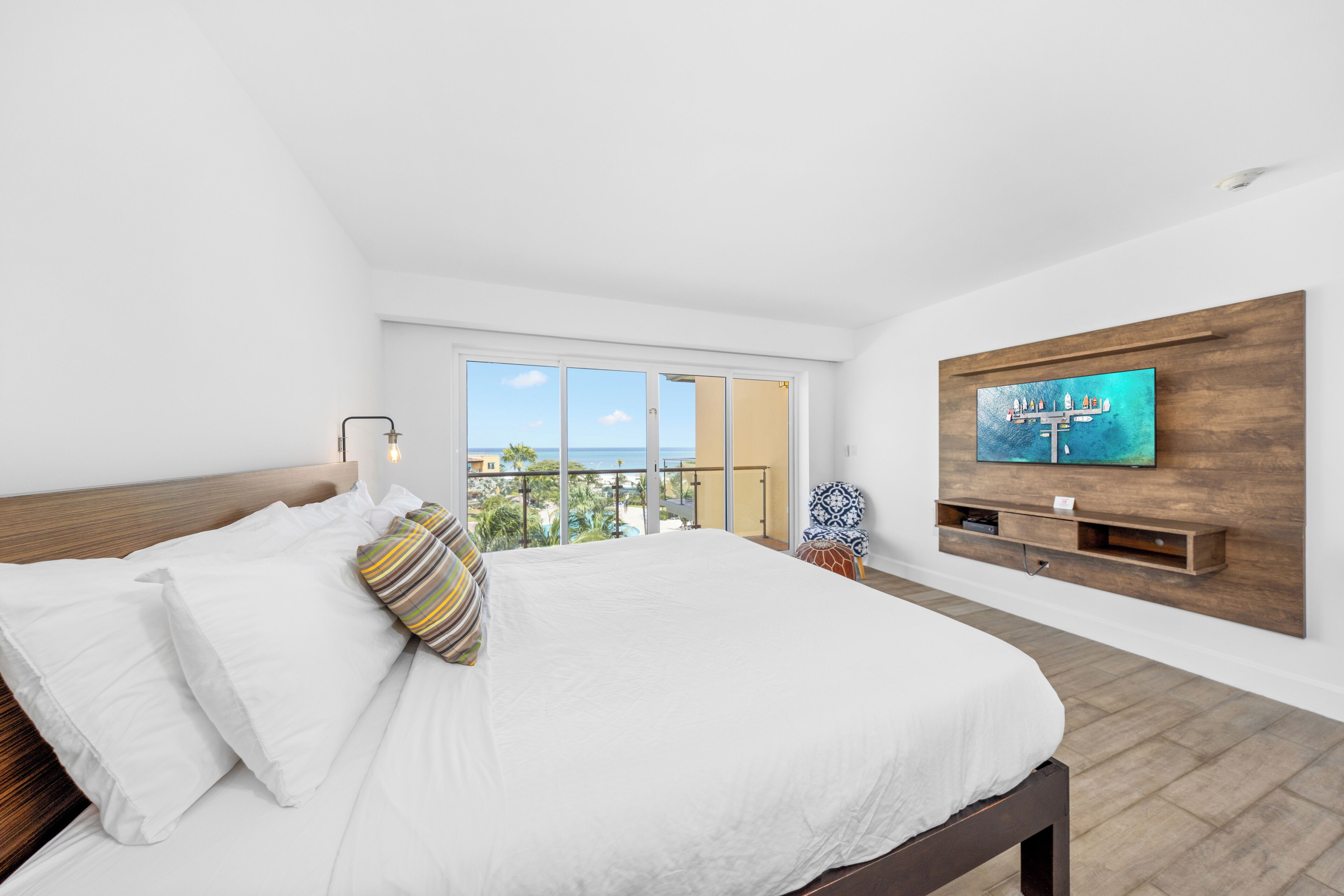 Ein modernes Schlafzimmer mit einem großen Bett, einem an einer Holzwand montierten Fernseher und einem Balkon mit Blick.