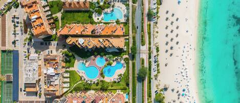 Vista aérea de um resort com várias piscinas, uma praia e uma área de estacionamento.