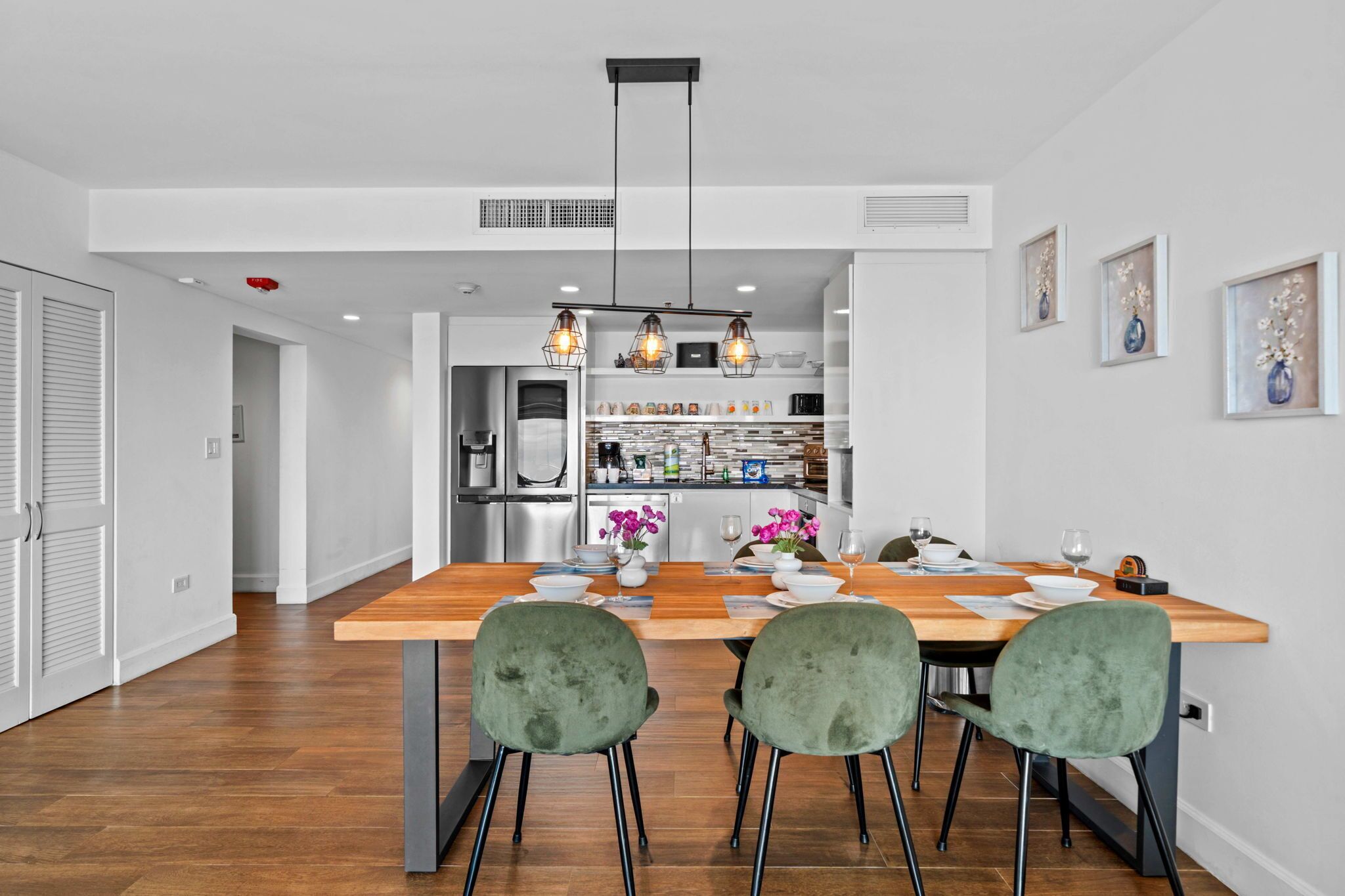 A modern kitchen with a central island, wooden dining table, and green chairs.