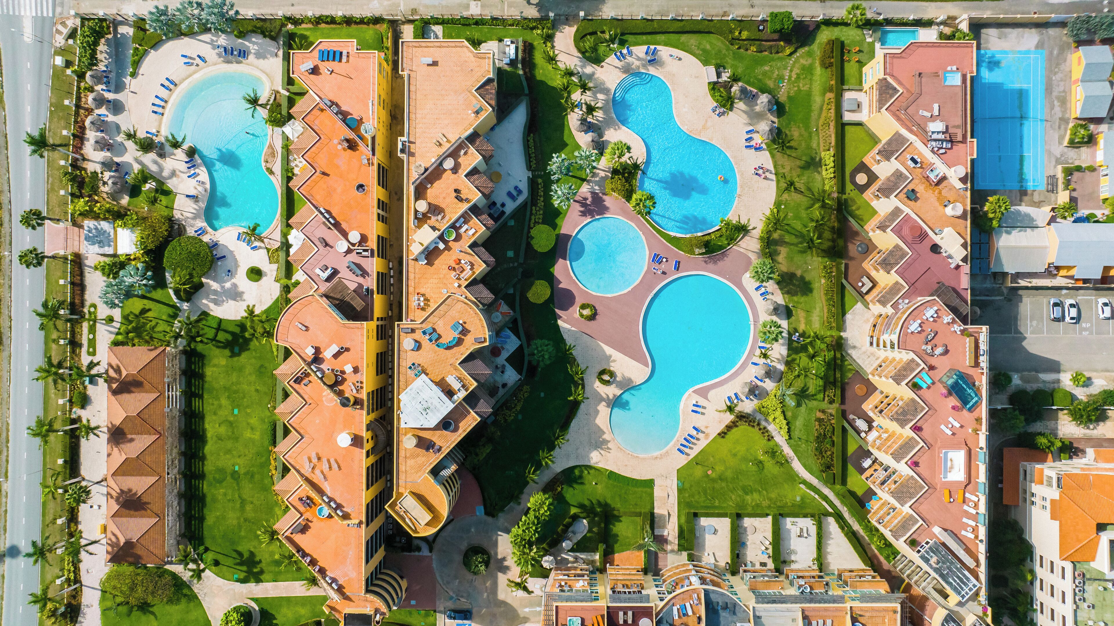 An aerial view of a resort with multiple swimming pools, sun loungers, and a well-maintained lawn.