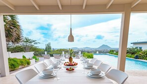 A dining table set for six with white chairs, a pool, and a mountain view.