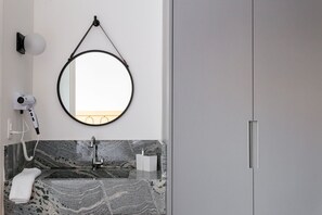 A modern bathroom with a marble sink, a round mirror, a hairdryer, and a towel. - Studios Mackenzie - Consolação (São Paulo)