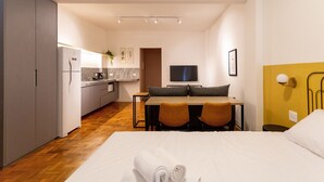 Habitación de hotel con cama, escritorio con sillas, televisor y kitchenette.