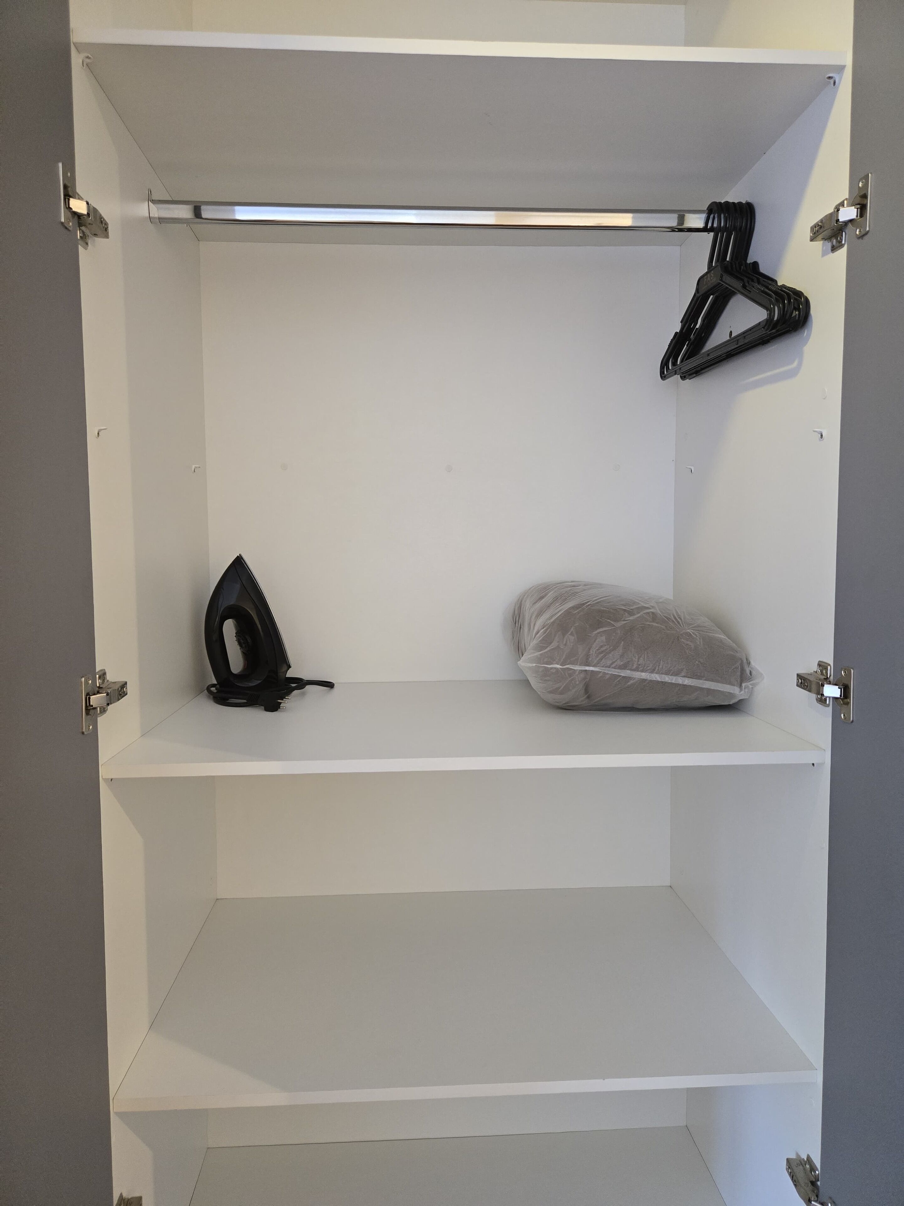 Ein weißer Kleiderschrank mit drei Einlegeböden, einer Kleiderstange und einer Tür mit silbernem Griff.