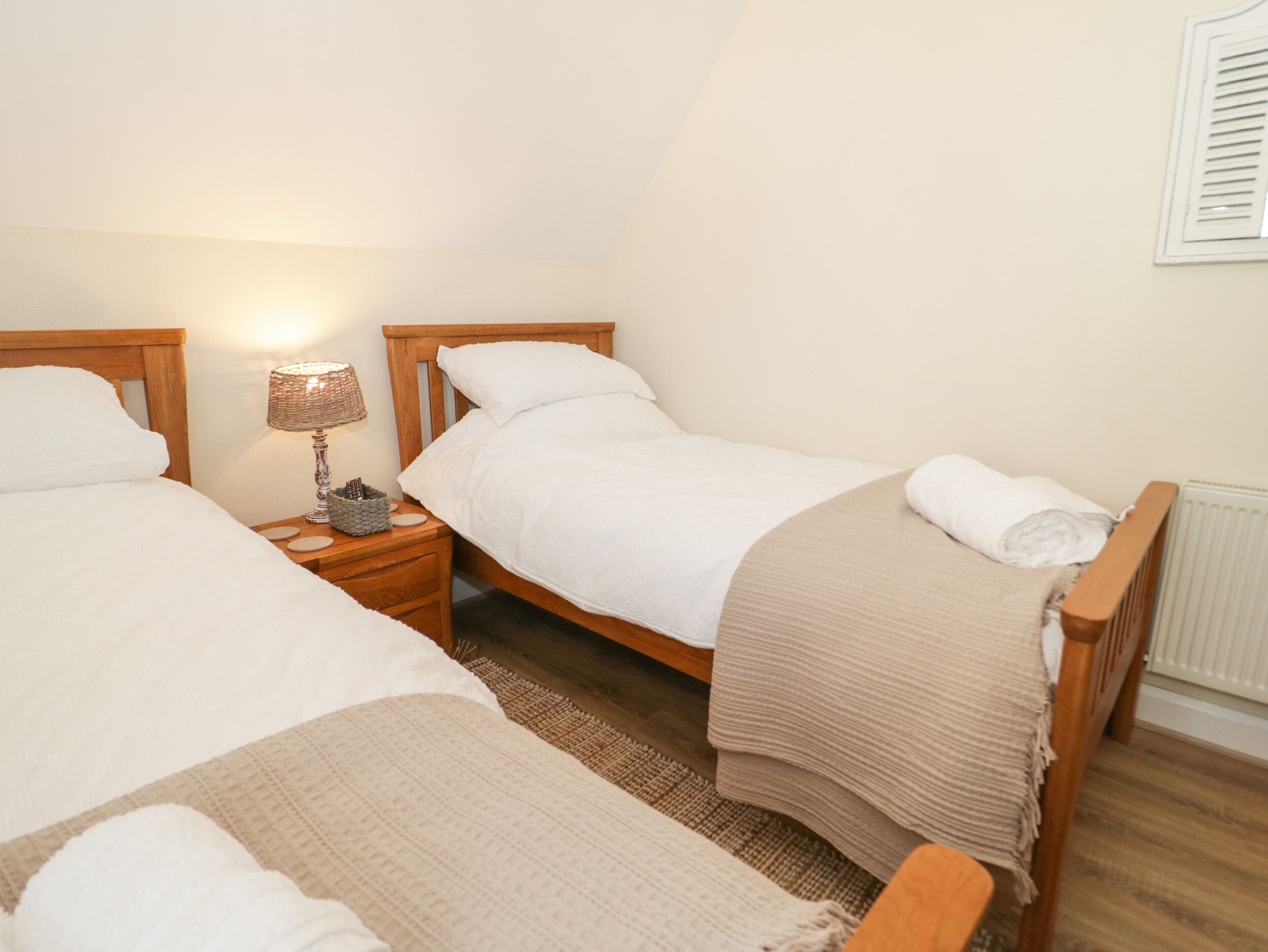 A bedroom with two single beds, a bedside table with a lamp, and a radiator.