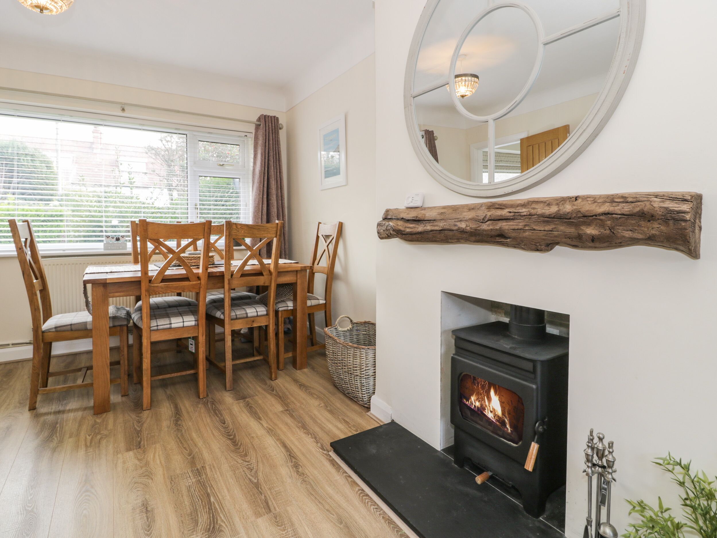 A dining area with a wooden table and chairs, a fireplace, and a round mirror on the wall.