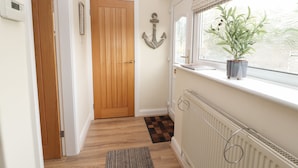 A hallway with a wooden door, a radiator, a window with a plant, and a rug. - Hilltops (Conwy)