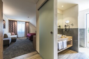 Een hotelkamer met een slaapbank, een bed, een badkamer met een wastafel en spiegel, en een douche.