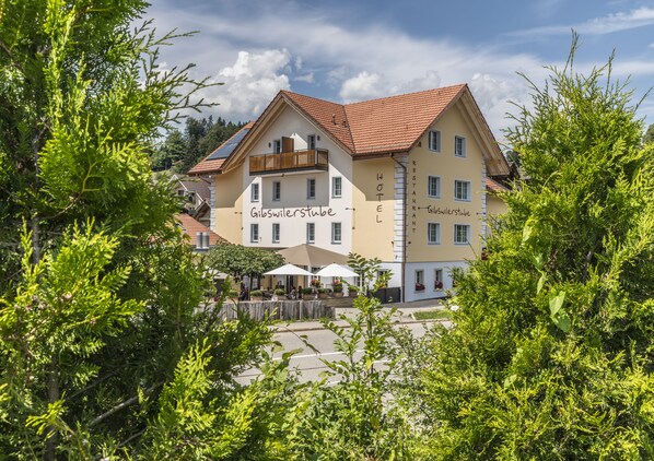 Een hotel met een bord waarop 'Gibswilerstube HOTEL RESTAURANT' staat, met terras en parasols.