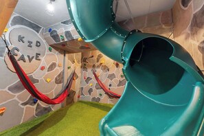 Un espace de jeux pour enfants avec un mur d’escalade, un toboggan et un hamac.