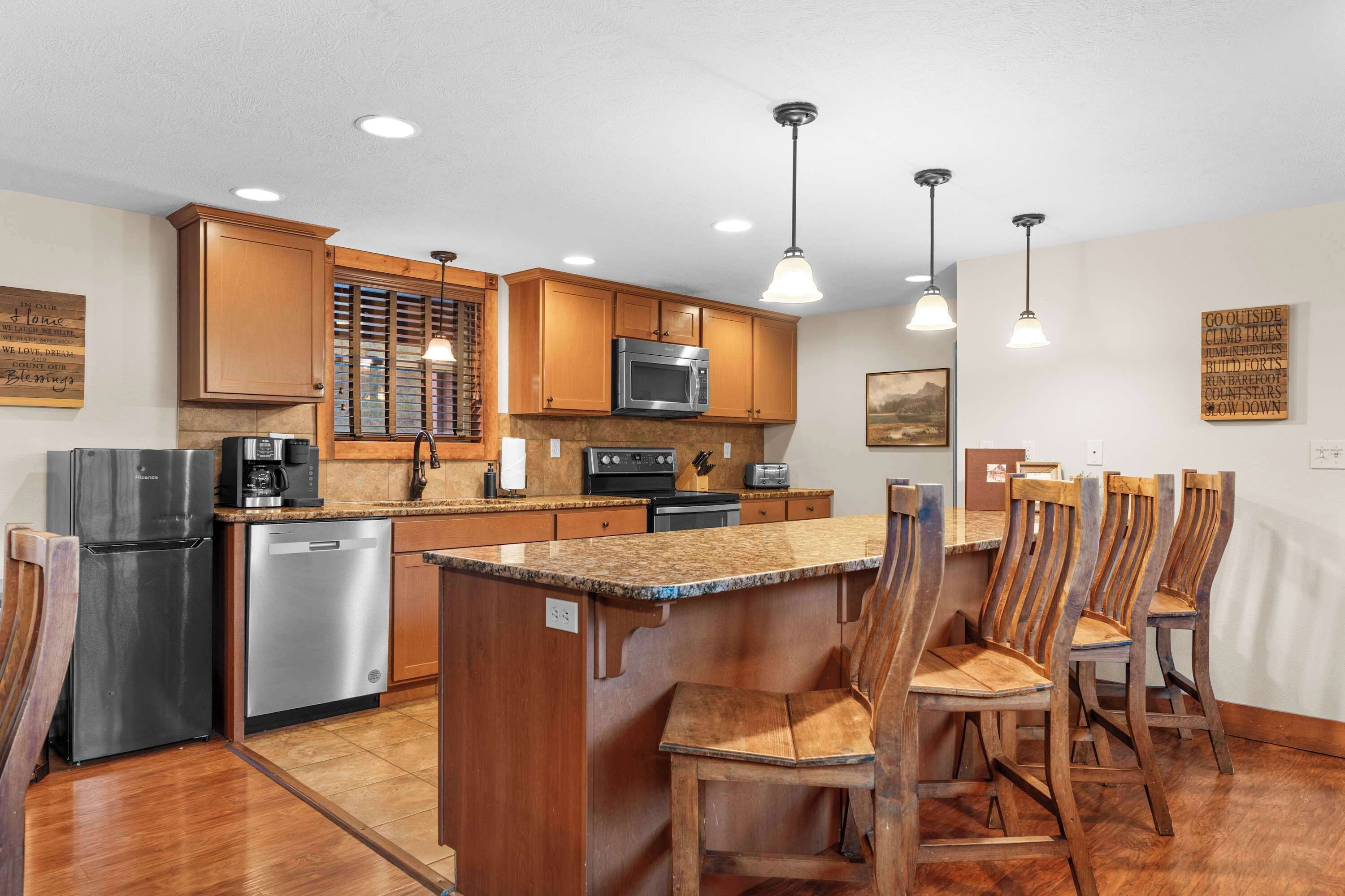 A kitchen with wooden cabinets, a stainless steel refrigerator, a dishwasher, a microwave, a stove, and a dining area with wooden chairs.