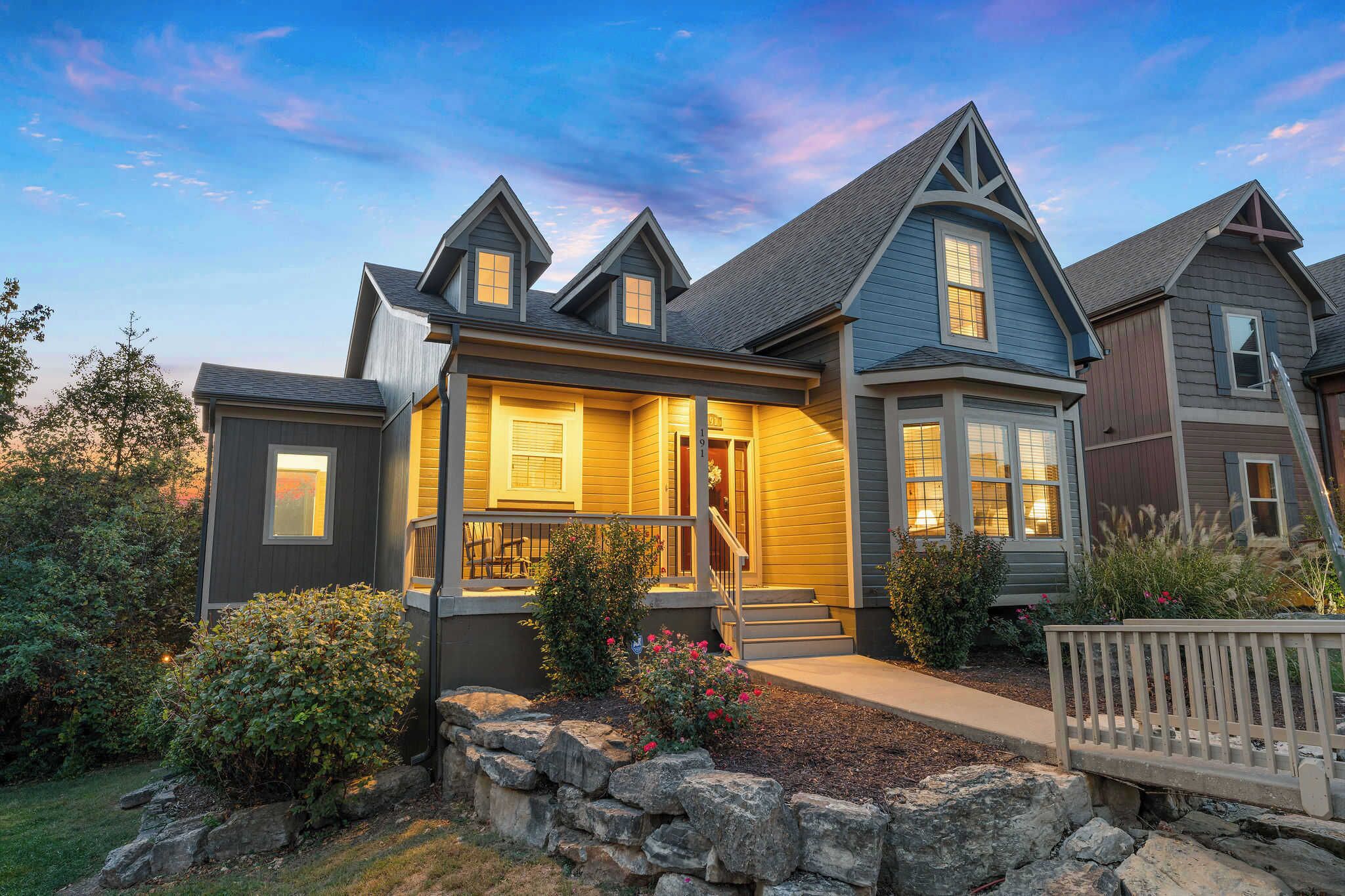 A two-story house with a porch, stone foundation, and a well-maintained garden.