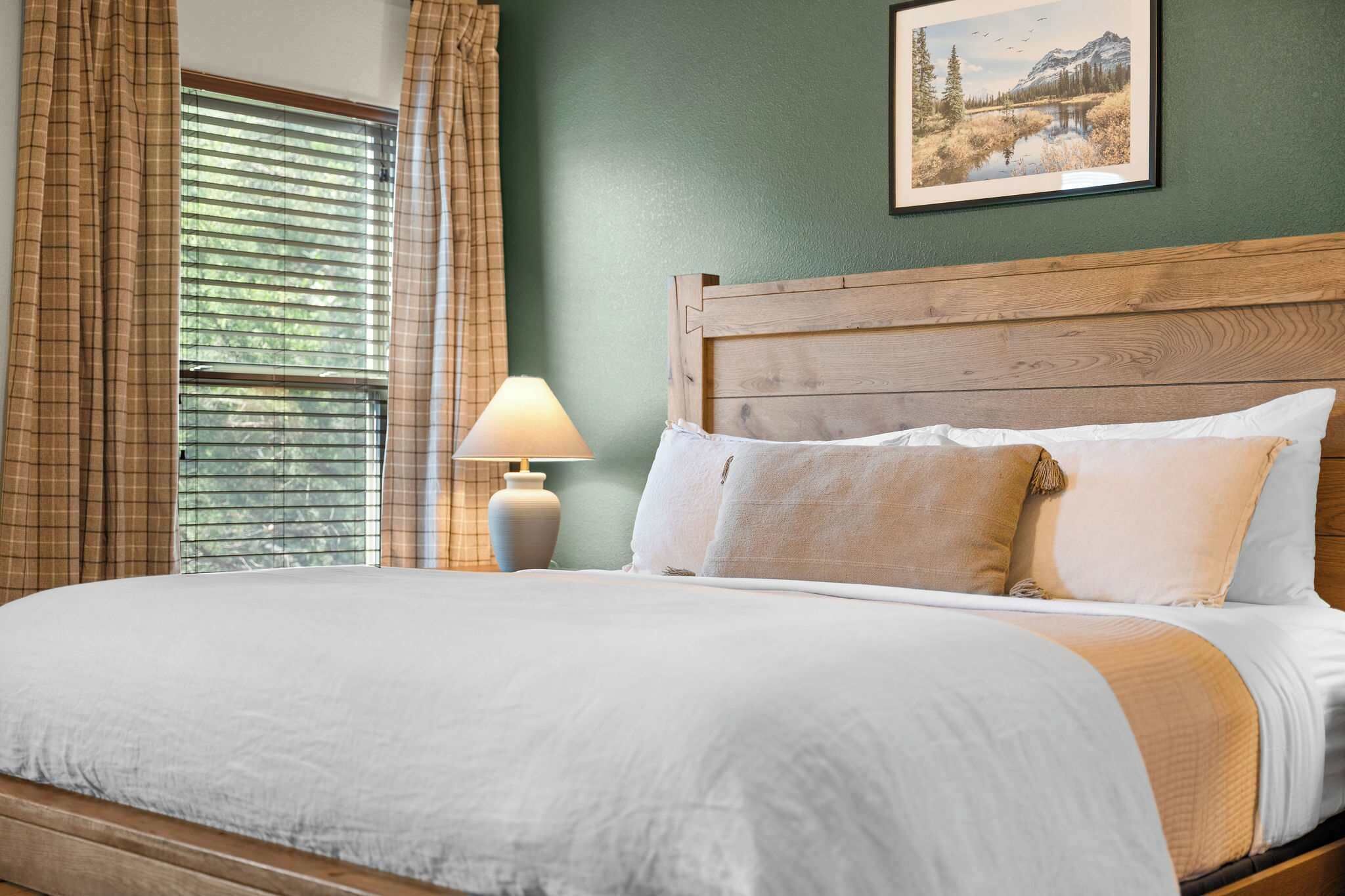 A neatly made bed with a wooden headboard, a bedside lamp, and a framed picture on the wall.