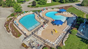An aerial view of a resort with two large swimming pools, sun loungers, umbrellas, and a fenced deck area.