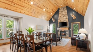 Un comedor con una mesa y sillas de madera, chimenea y pared de piedra con un ciervo montado.