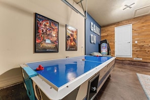 A pool table with a blue felt surface, a 'GAME ON' sign, and two movie posters on the wall.