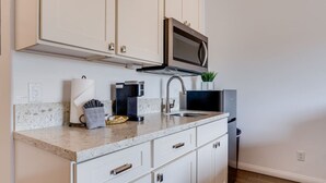 A modern kitchen with white cabinetry, a built-in microwave, a coffee maker, and a sink. - Waena Inn #14 Private Studio w/2 queen beds (Wailuku)
