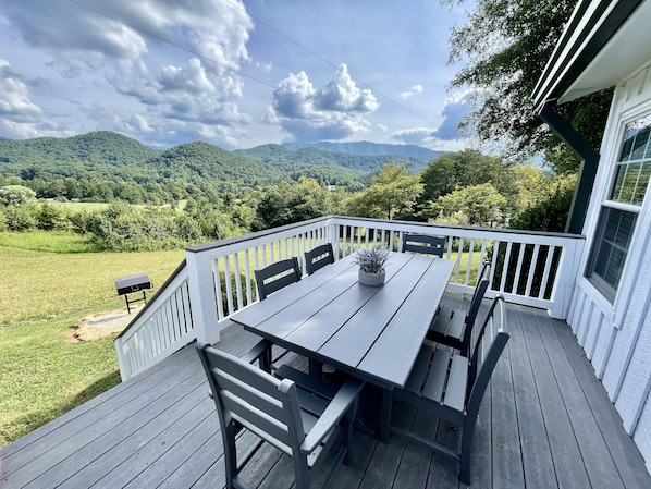 Enjoy outdoor dining on the deck with a table and chairs, surrounded by a lush green landscape and rolling hills.