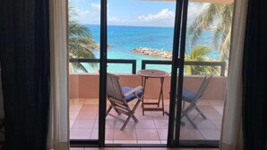 A balcony with a view of the ocean, two chairs, and a small table. - Beachfront Condo at Club de Yates (Puerto Aventuras)