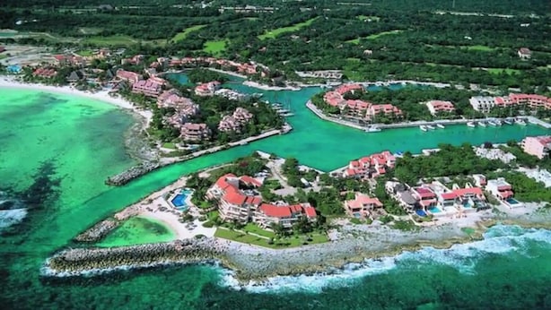 An aerial view of a coastal resort with multiple buildings, clear turquoise waters, and a beach area. - Beachfront Condo at Club de Yates (Puerto Aventuras)