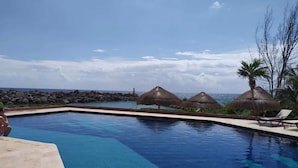A swimming pool with clear blue water, surrounded by lounge chairs and thatched umbrellas. - Beachfront Condo at Club de Yates (Puerto Aventuras)