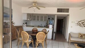A dining area with a round table and chairs, a ceiling fan, and a kitchen in the background. - Beachfront Condo at Club de Yates (Puerto Aventuras)