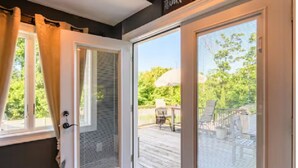 Vue depuis une porte-fenêtre coulissante sur une terrasse en bois, avec des meubles d’extérieur et un ciel dégagé.