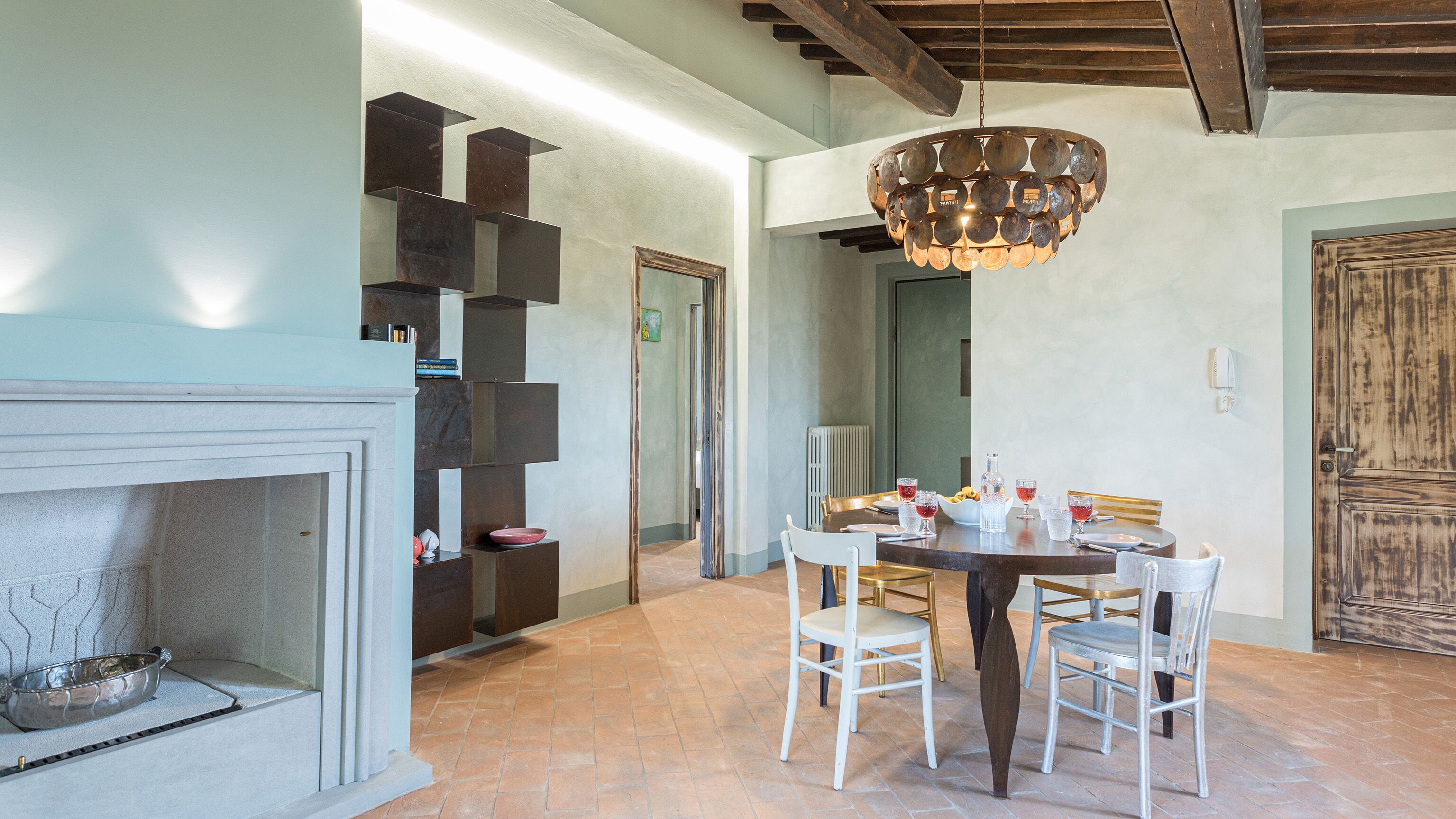 Un coin repas avec une table ronde, des chaises blanches, un lustre et une cheminée.