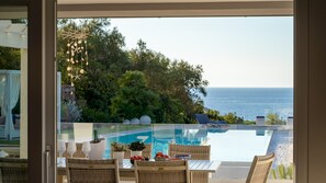 A poolside area with a view of the ocean, outdoor furniture, and a decorative hanging light fixture.
