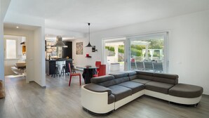 Eine moderne Küche mit Steinrückwand, ein Essbereich mit roten Stühlen und ein großes Fenster mit Blick auf einen Garten.