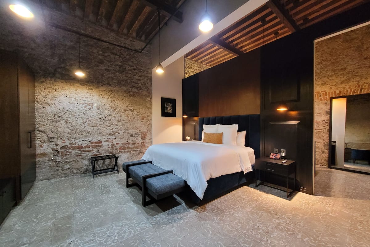 A modern bedroom with a large bed, a bench, a bedside table, and a mirror.
