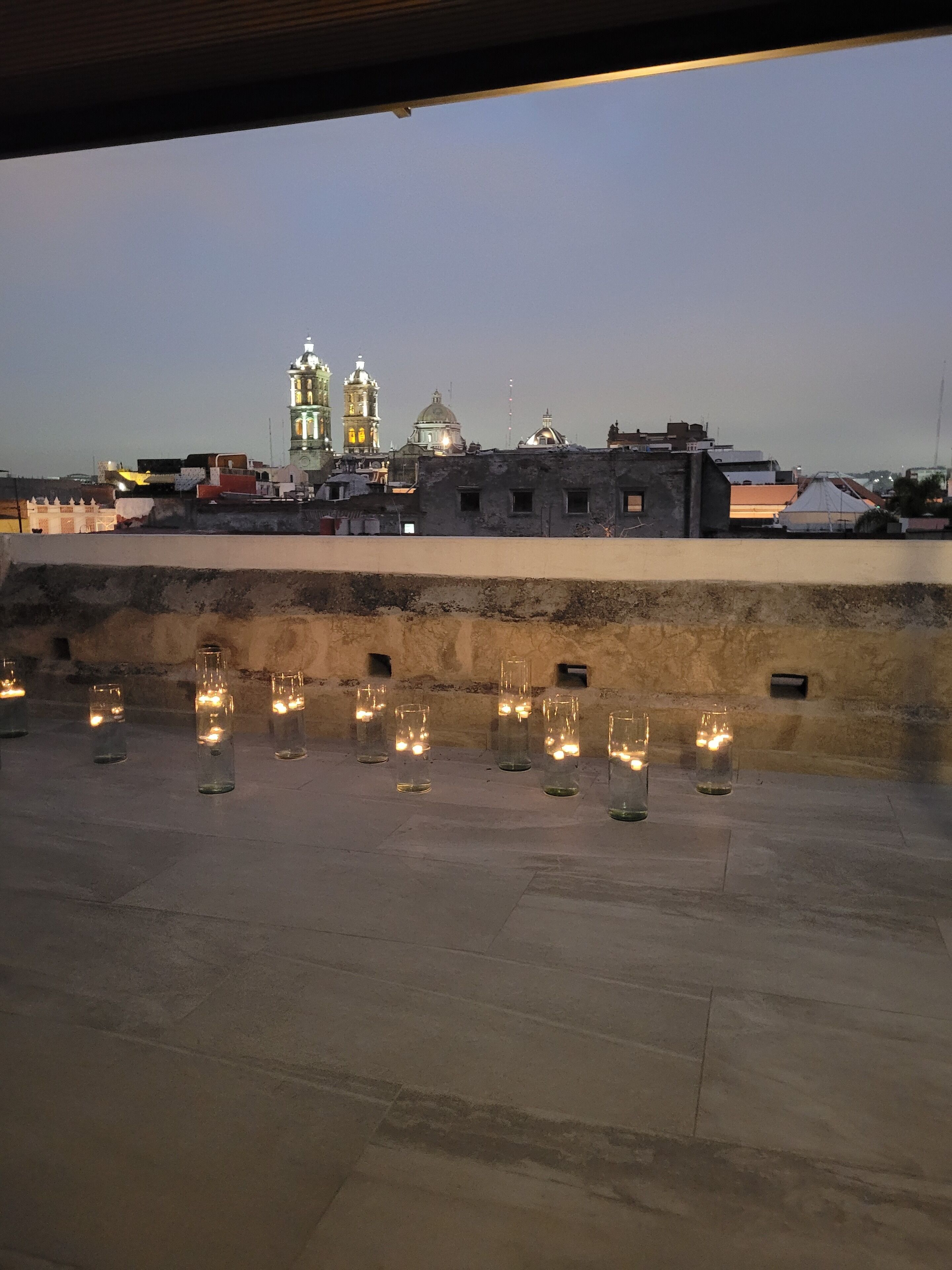 A rooftop terrace with a row of lit candles, a view of a historic building with domes, and a clear sky.