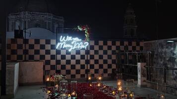 A romantic outdoor setting with a neon sign reading "Will you marry me?" surrounded by candles and rose petals.