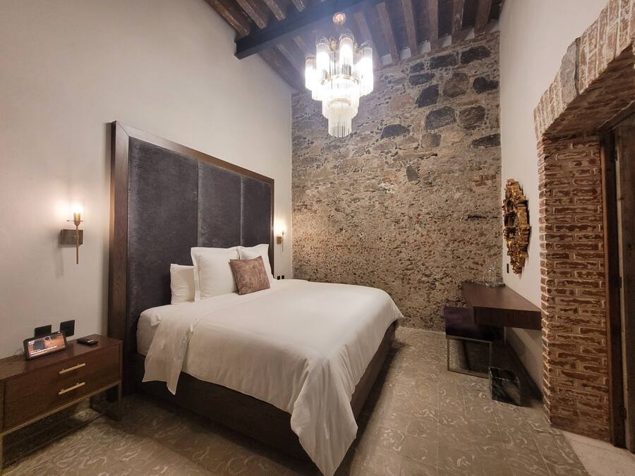 A bedroom with a stone wall, a wooden headboard, a chandelier, and a nightstand with a clock.