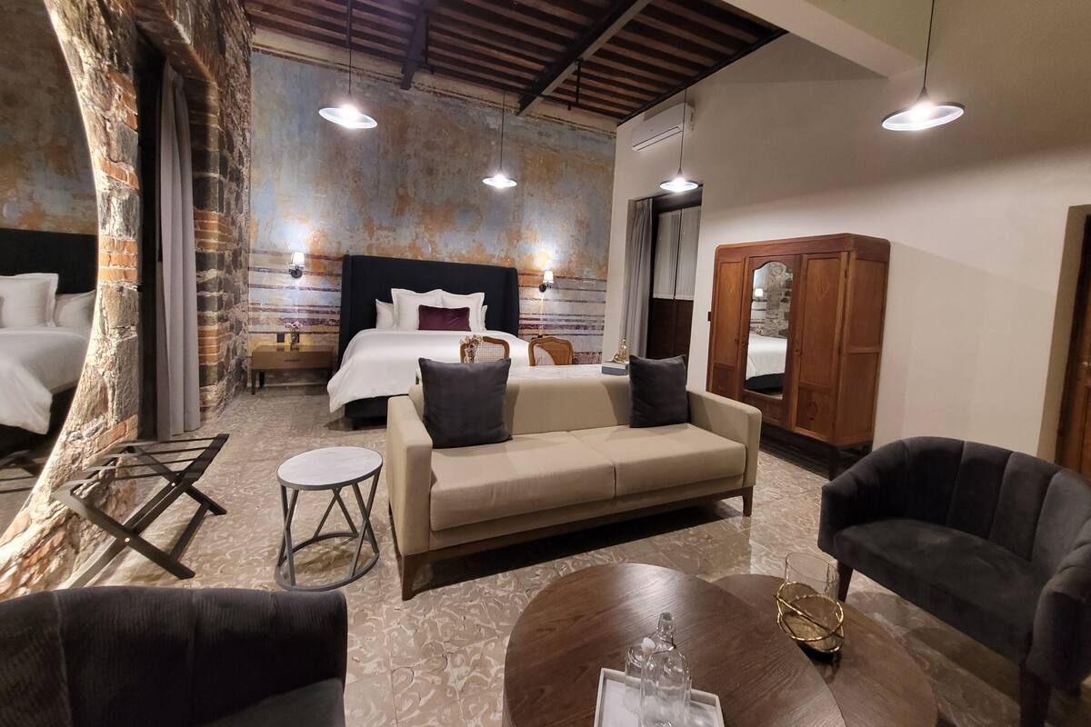 A hotel room with a large bed, a sofa, a coffee table, and a wardrobe.