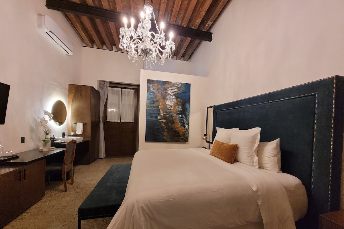 A bedroom with a large bed, a desk with a chair, a vanity with a mirror, and a chandelier.